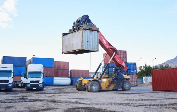 Montacargas de gran capacidad manipula contenedores en una terminal de logística y transporte, facilitando el movimiento eficiente de mercancías.